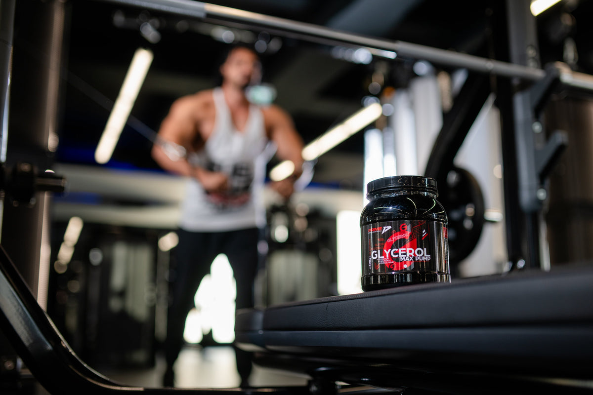 Cutie de Glycerol Max Pump pe o bancă de sală, cu un sportiv în maiou alb, neclar, în fundal